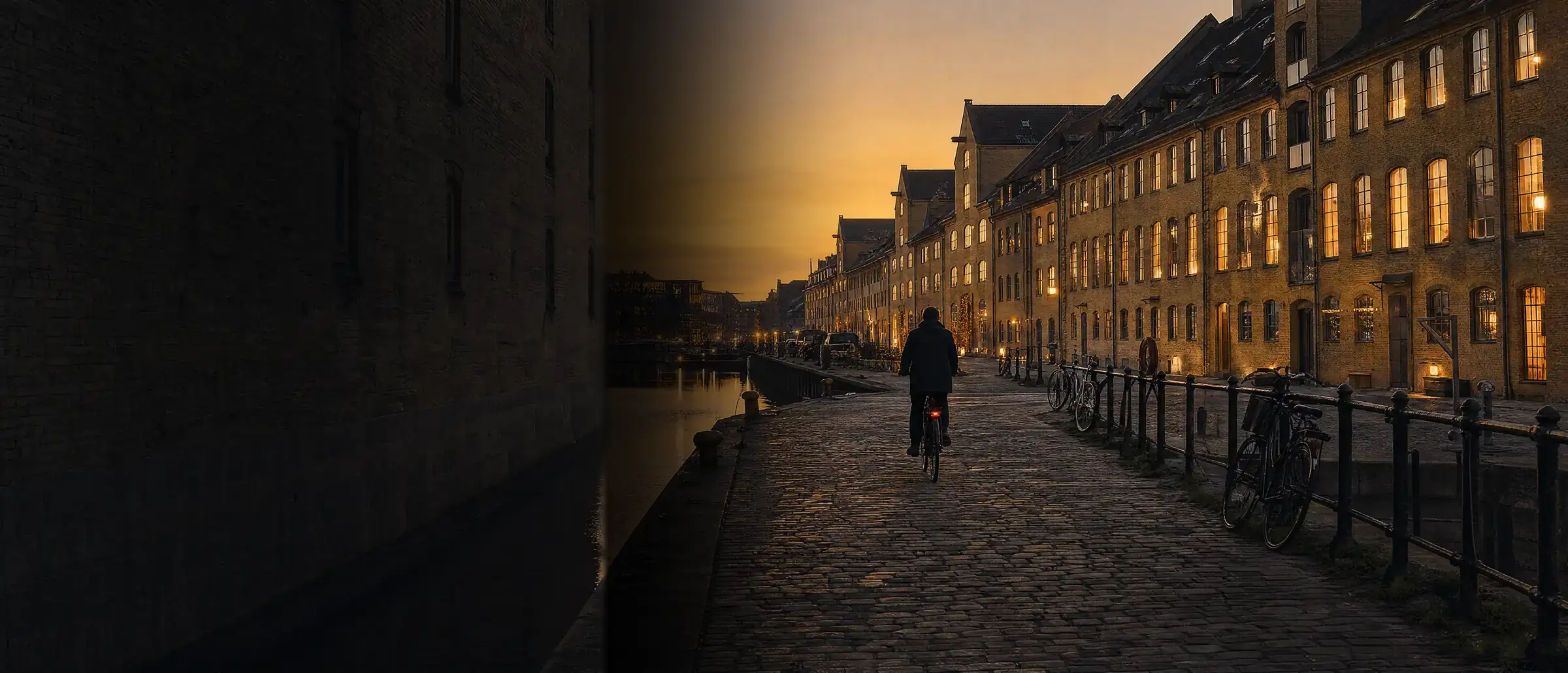 En havnekaj i København en aften: en cyklist på brostenene langs vandet og gamle pakhuse med oplyste vinduer.